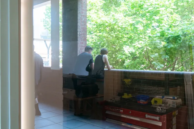The back of two people leaning toward the balcony wall viewed through the glass window.