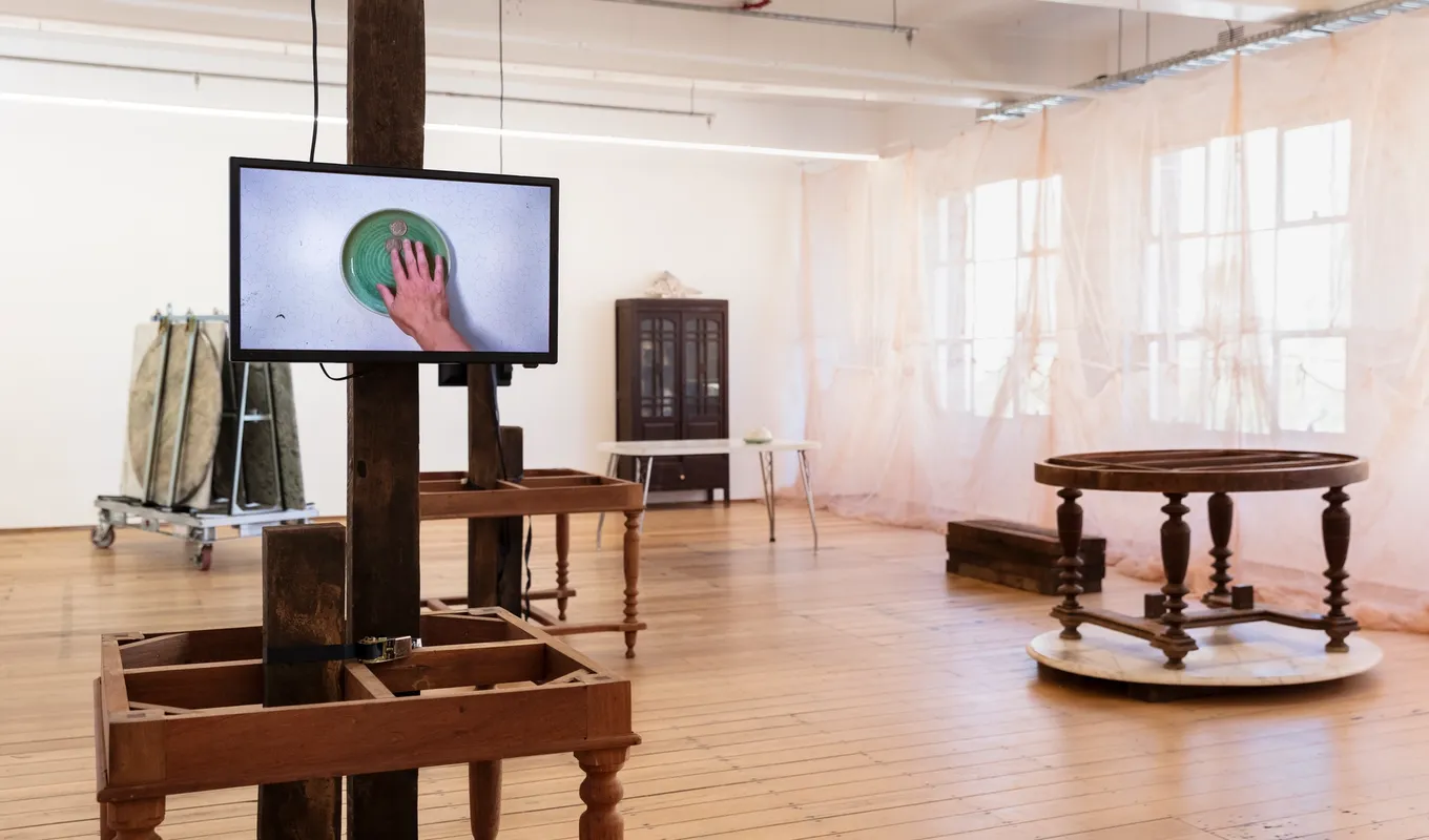 Videos displaying on wooden table, mosquito nets against the windows, marble tables, and cabinet at the 'Inheritance' exhibition.