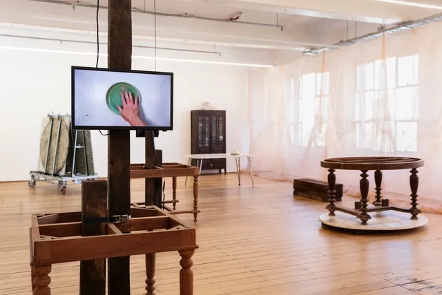 Videos displaying on wooden table, mosquito nets against the windows, marble tables, and cabinet at the 'Inheritance' exhibition.