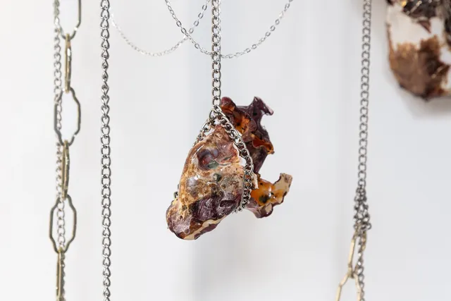 Two marbled sculptures and silver chains of different link sizes. The sculpture in the middle is hang by a silver chain.