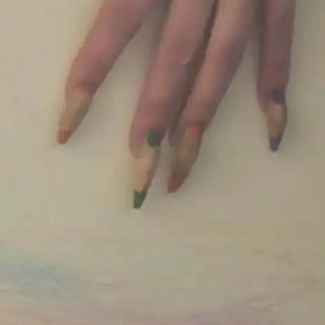 A detail shot of four fingers with long ballerina shaped acrylic nails. The nails are painted a beige tone with two coloured dots on each end of the nail.