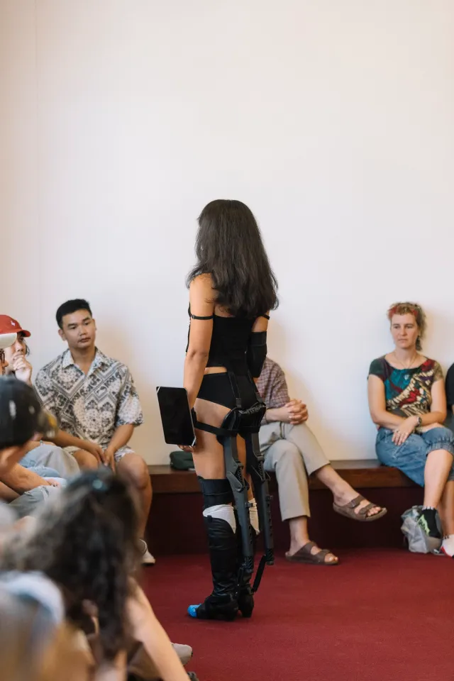 Ari performing standing on burgundy carpet facing a crowd watching her.