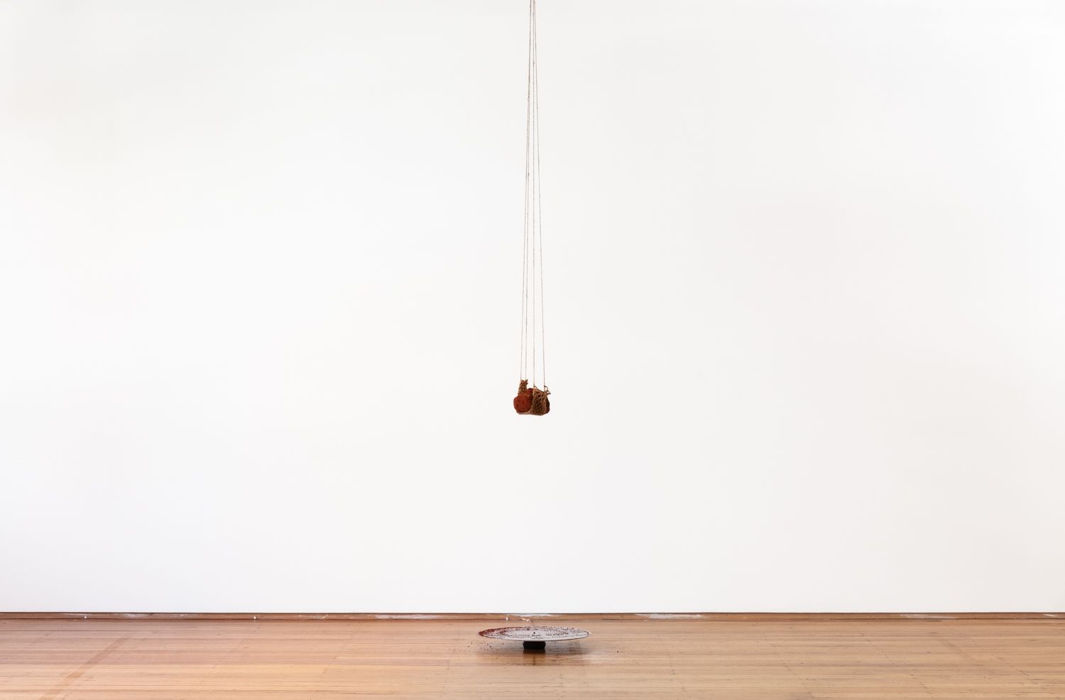 A piece of earth hangs from some rope from the ceiling, dangling above a circular metal plate that has collected some of the fallen residue.