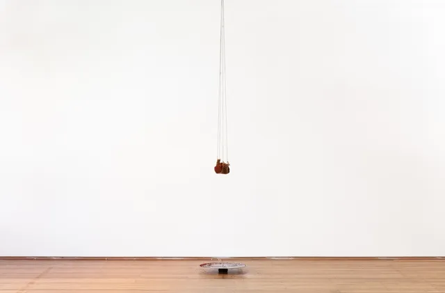 A piece of earth hangs from some rope from the ceiling, dangling above a circular metal plate that has collected some of the fallen residue.