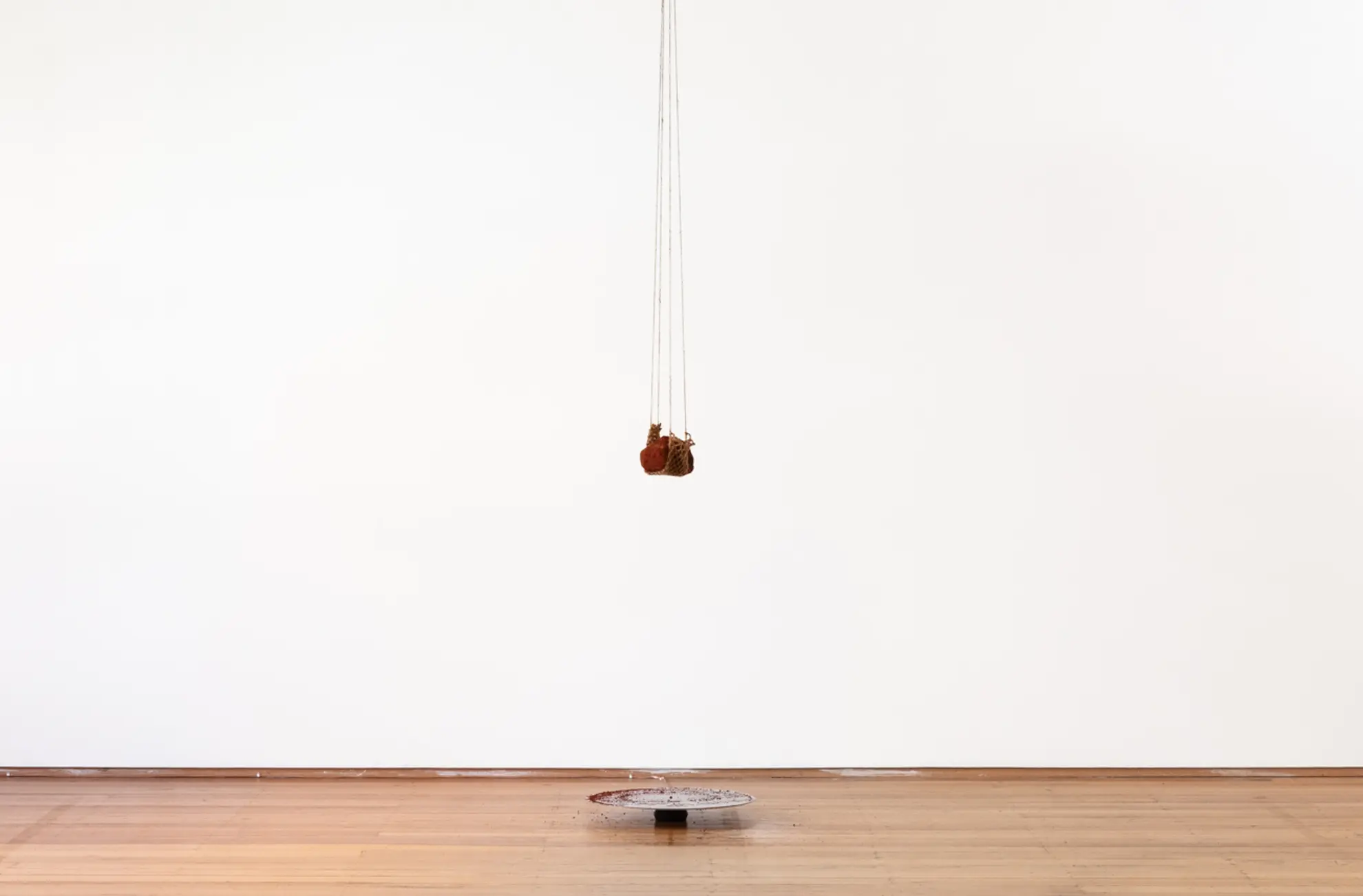 A piece of earth hangs from some rope from the ceiling, dangling above a circular metal plate that has collected some of the fallen residue.