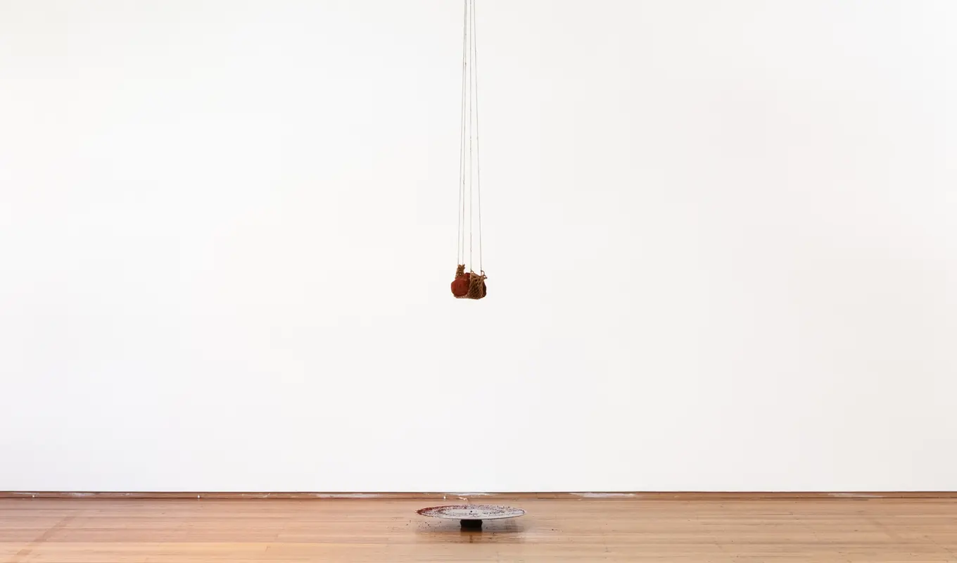 A piece of earth hangs from some rope from the ceiling, dangling above a circular metal plate that has collected some of the fallen residue.