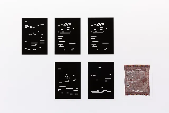 Installation view of five blackout texts with some broken-up white fragments of text exposed, three are placed on the top and two on the bottom with an embroidered map shawl on the bottom right row.