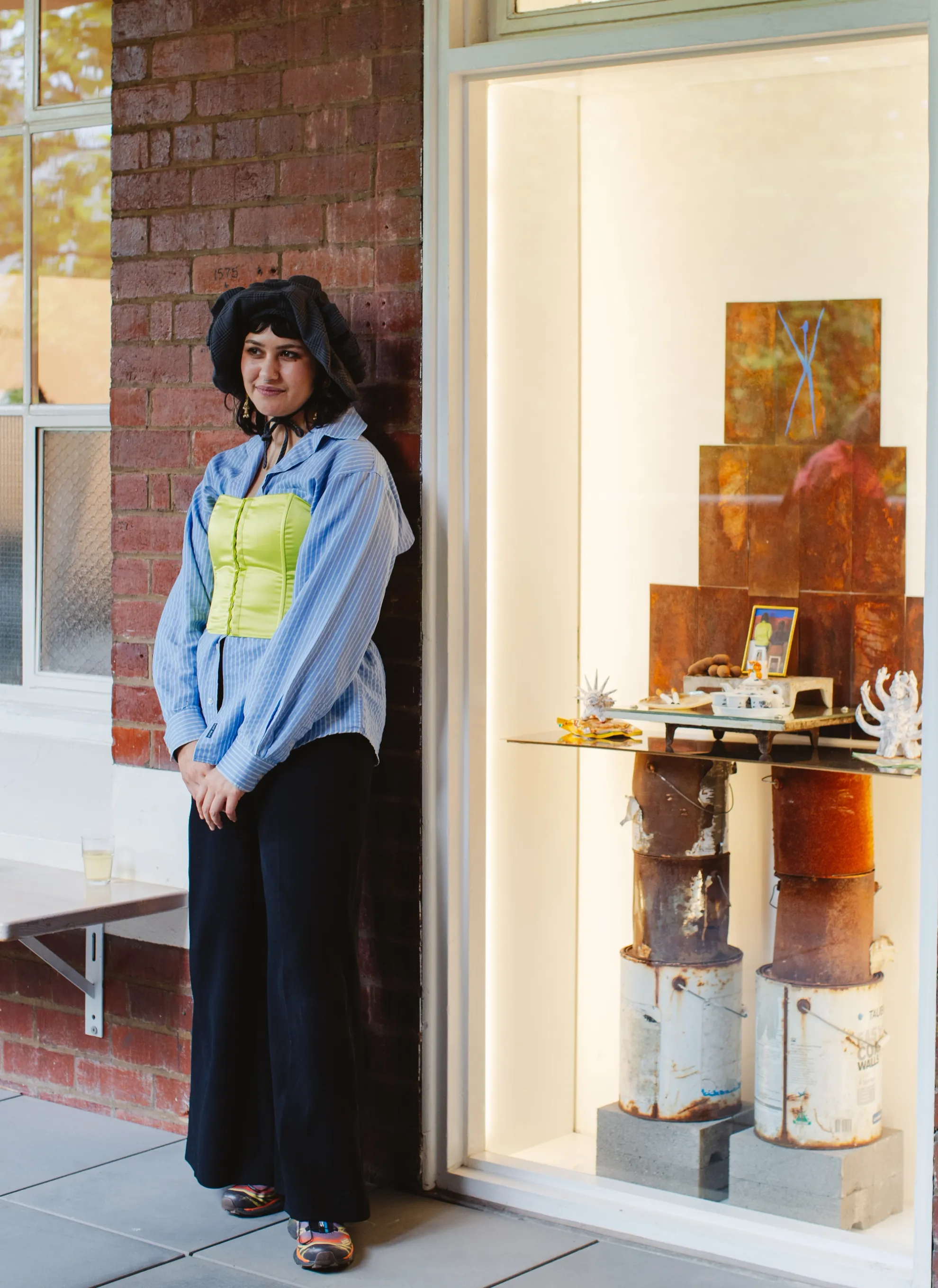 A person stands next to a brick wall and a display window with various objects inside.