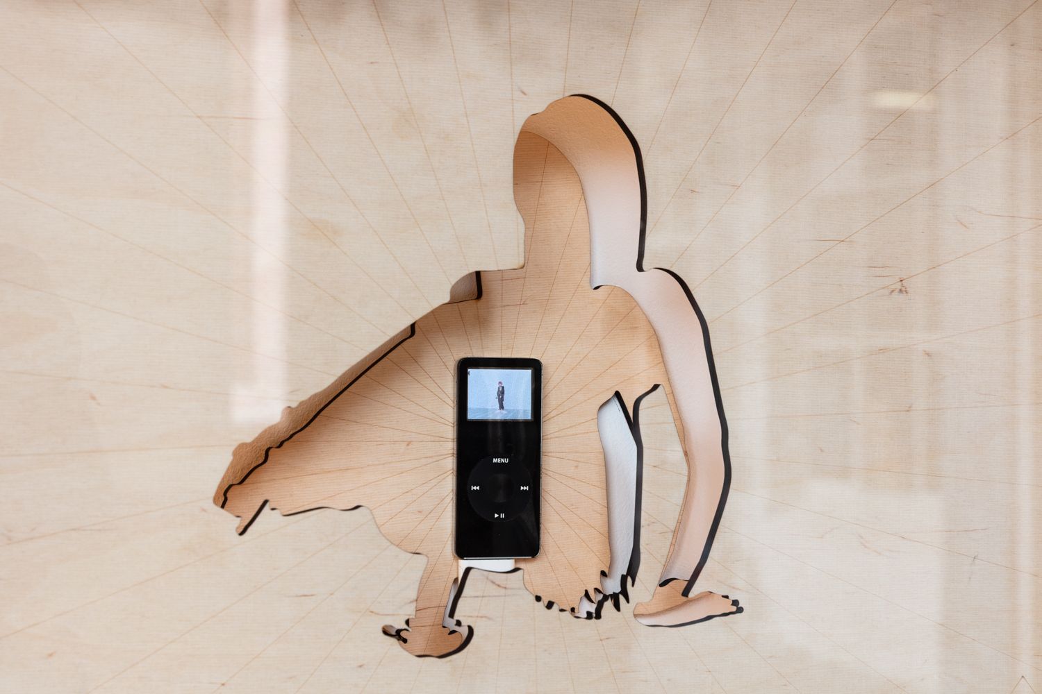 Close-up of a contorted figure laser-cut out of wooden sheets and transformed into two seperate layers. One in front of the other with an iPod placed in the centre of the figure showing a video.