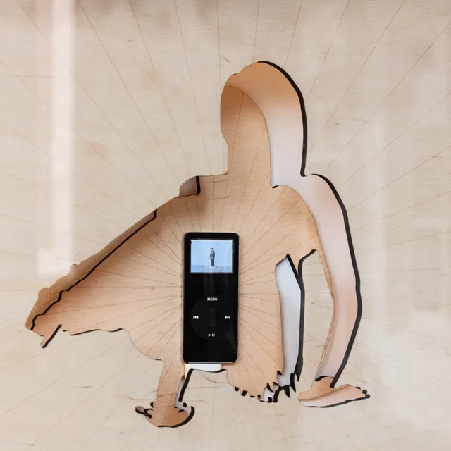 Close-up of a contorted figure laser-cut out of wooden sheets and transformed into two seperate layers. One in front of the other with an iPod placed in the centre of the figure showing a video.