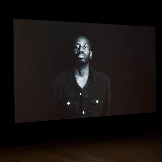 A large projection of a figure standing from the waist up. The film is in Black and White