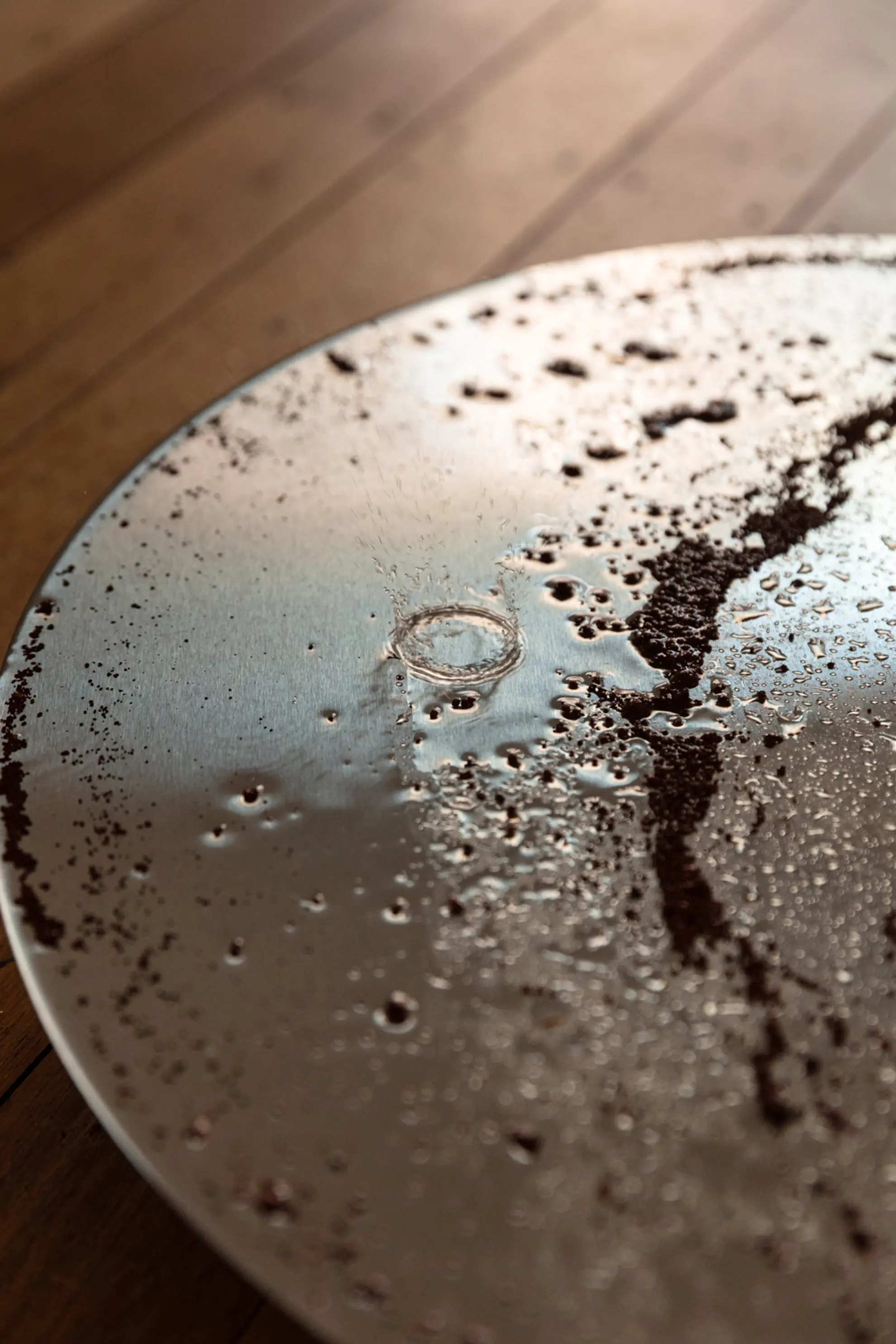 Close-up of a circular metal plate with earthy residue and water scattered across the surface.