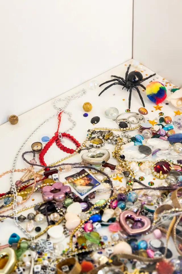 A detail from Matilda Davis' installation "I’ll Leave a Secret in the Window for You: Painting Grotto". The image shows an assortment of trinkets including love heart earrings, beads and gems.
