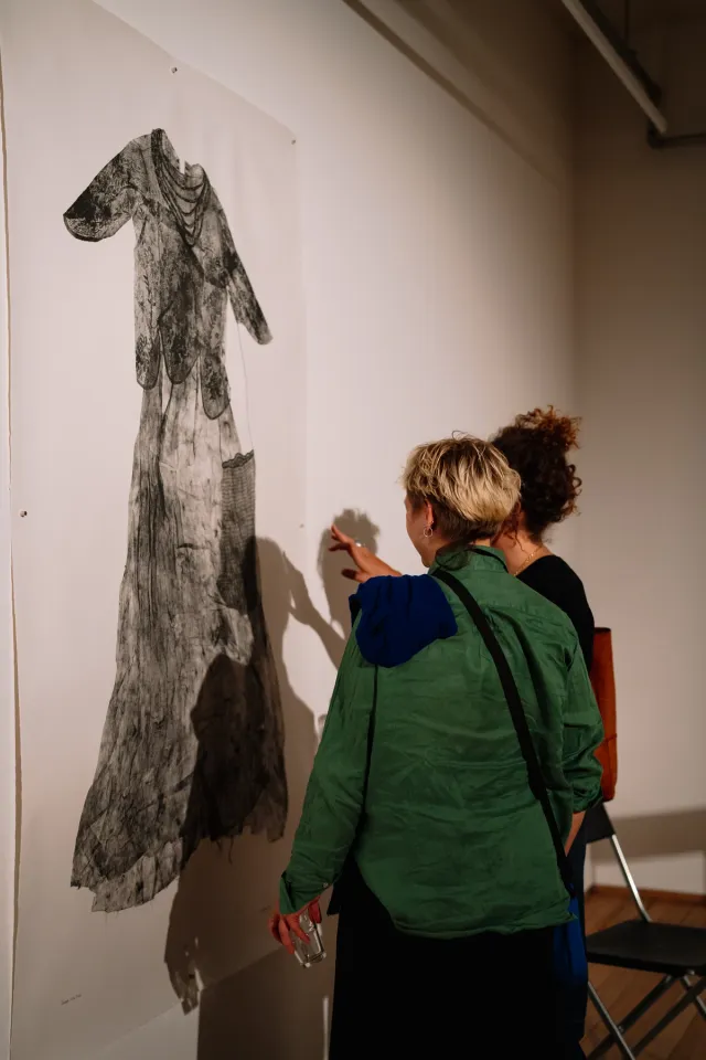 2 people stand in front of a large format print of a dress, they are in conversation about the work