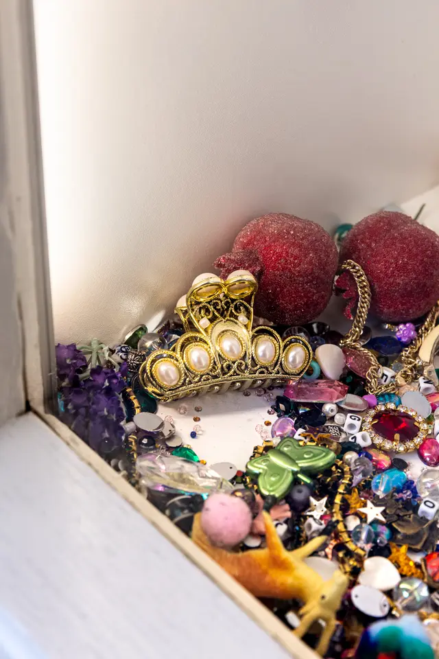 A detail from Matilda Davis' installation "I’ll Leave a Secret in the Window for You: Painting Grotto". The image shows an assortment of trinkets including fake fruit, butterflies, toy animals and gems.