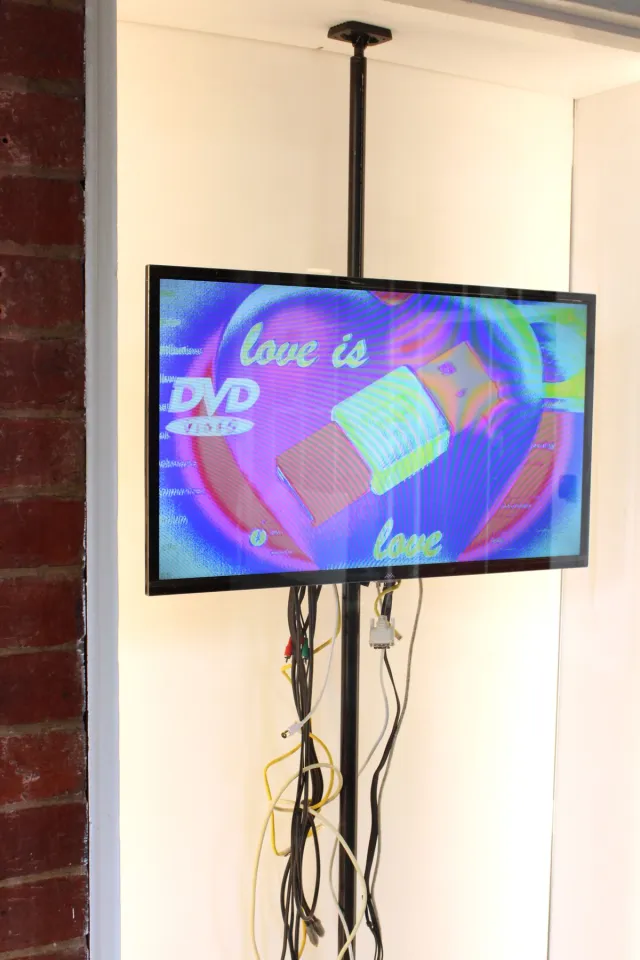 Behind a white framed window there is a tv displayed on a black pole. The screen shows a holographic with heart and usb motifs.