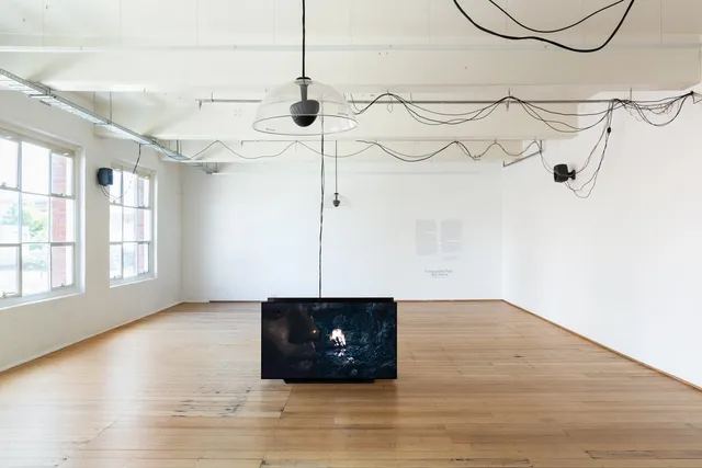 2 large screens stand on the floor of West Space Gallery. There are black cords that drape across the roof and all around the space.