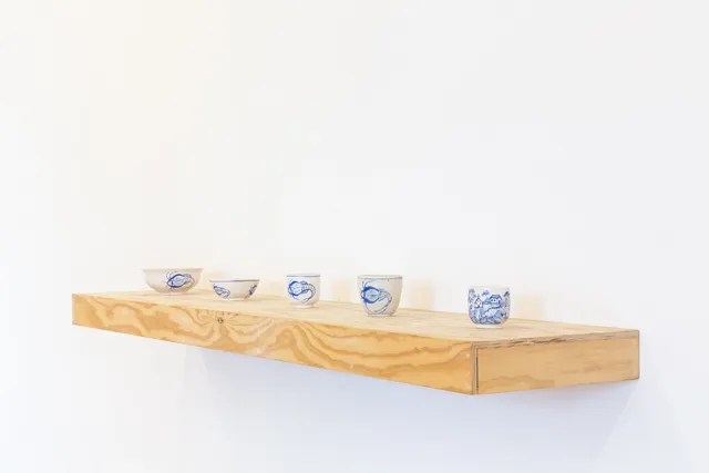5 small ceramic-like blue and cream coloured cups presented on a floating wooden shelf.