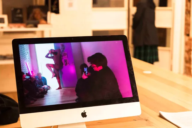 A mac computer sits on the desk in the West Space Office. On the screen we see a livestream performance and people watching.