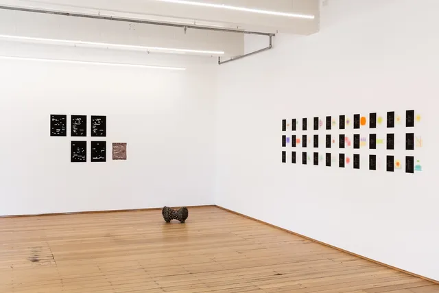 Two series of artworks hanging on the wall, a ceramic sculpture in the middle on the floor.