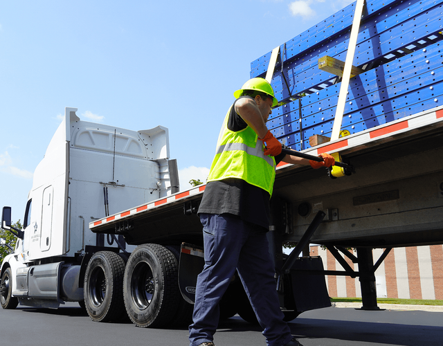 A worker strapping down equipment on the back of a semi truck