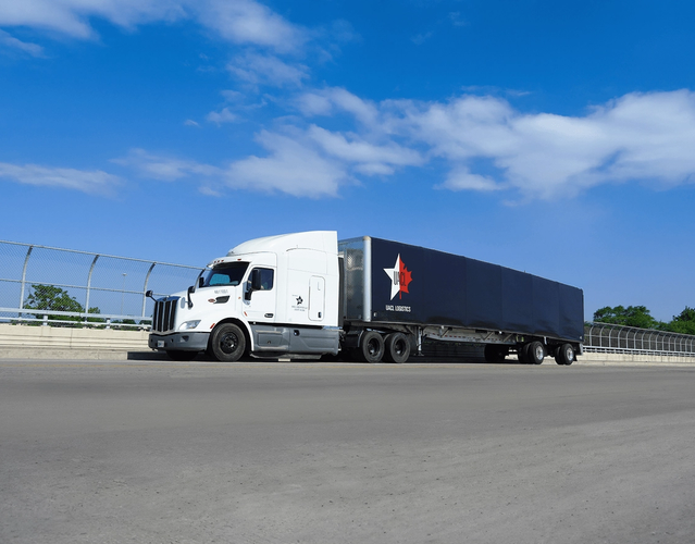 a white semi-truck with a black trailer featuring the UACL logo, driving on a highway