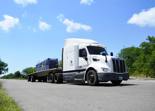 a white semi-truck with a flatbed trailer loaded with blue metal beams parked on a paved road