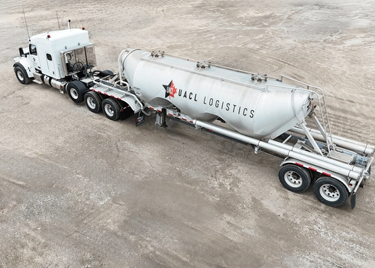 a white semi-truck with a cylindrical tanker trailer labeled "UACL Logistics" parked on a gravel surface