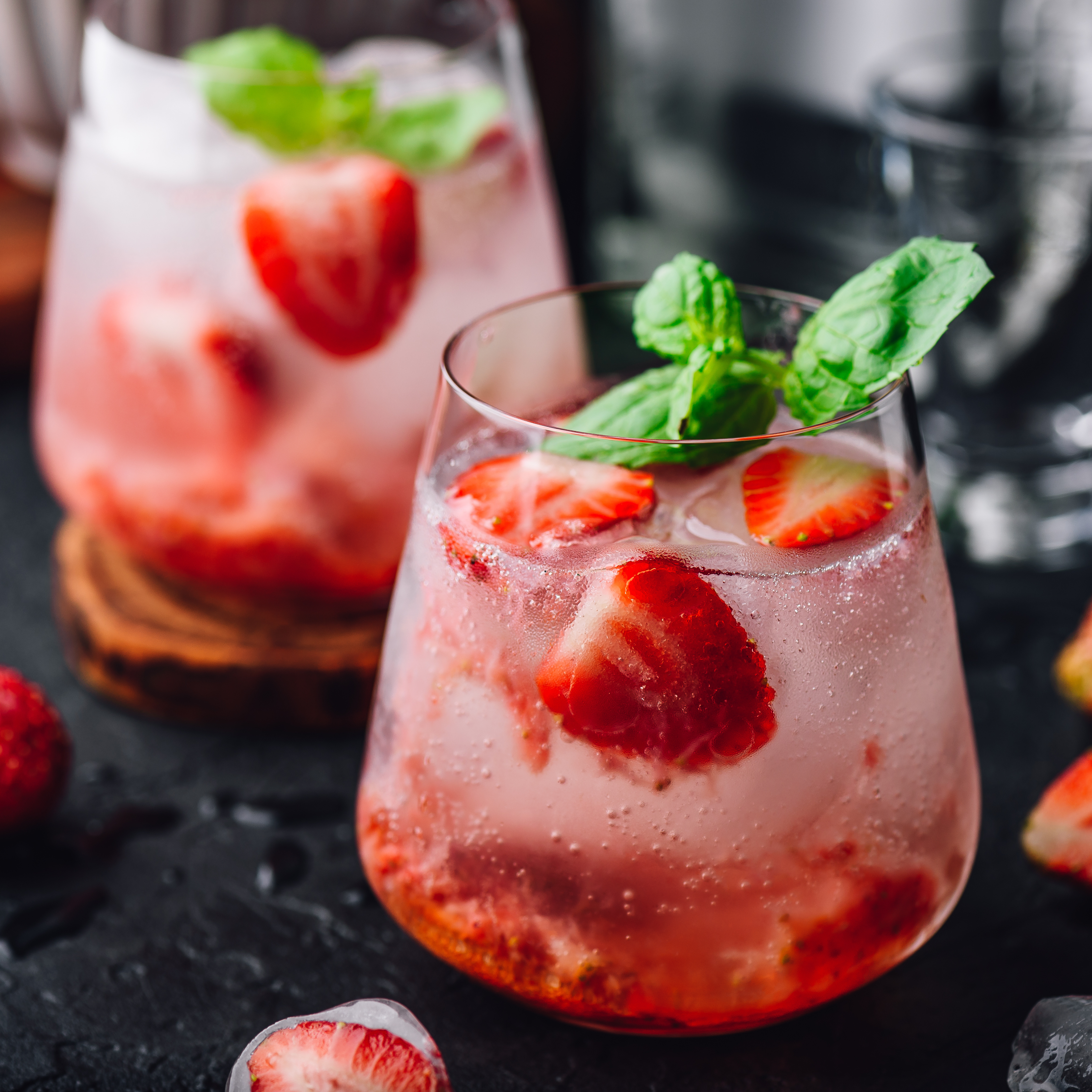 Close-up of two glasses filled with a refreshing strawberry cocktail garnished with mint leaves and ice cubes.