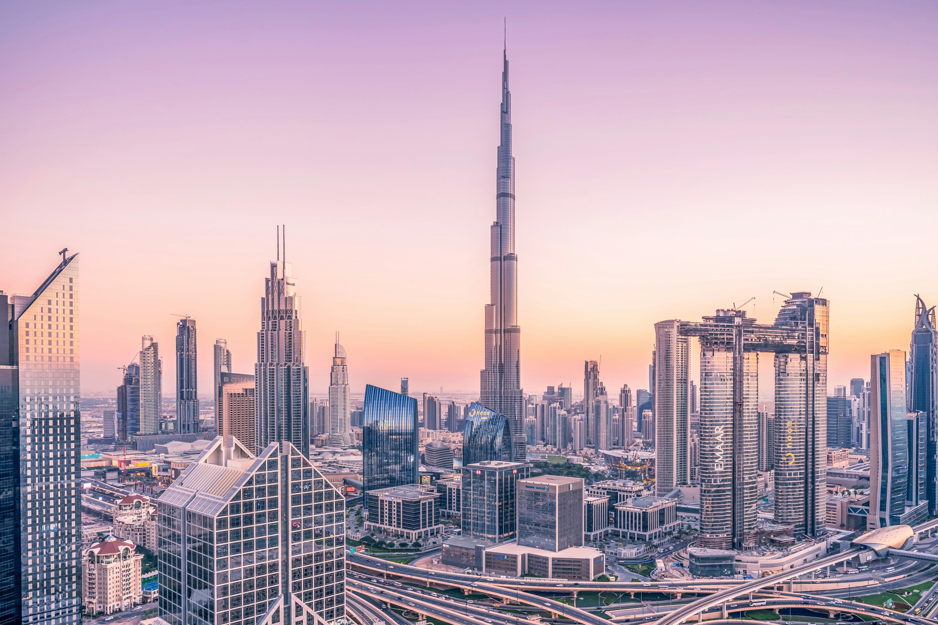 Dubai cityscape at sunset with the Burj Khalifa and other skyscrapers silhouetted against a purple and orange sky