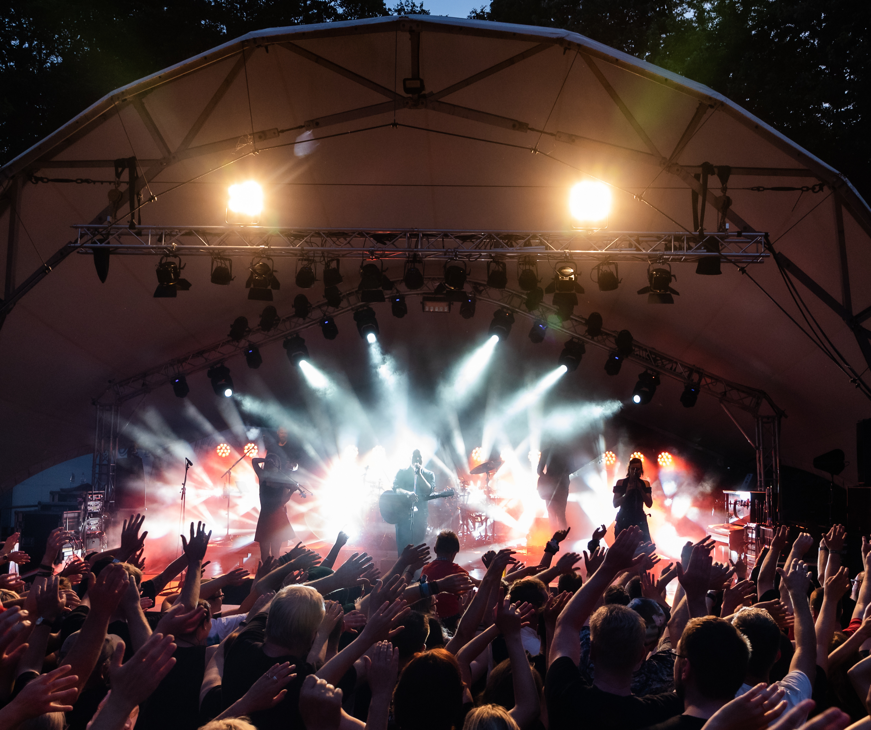 Band performing on stage with bright lights and a cheering crowd at an outdoor music concert.