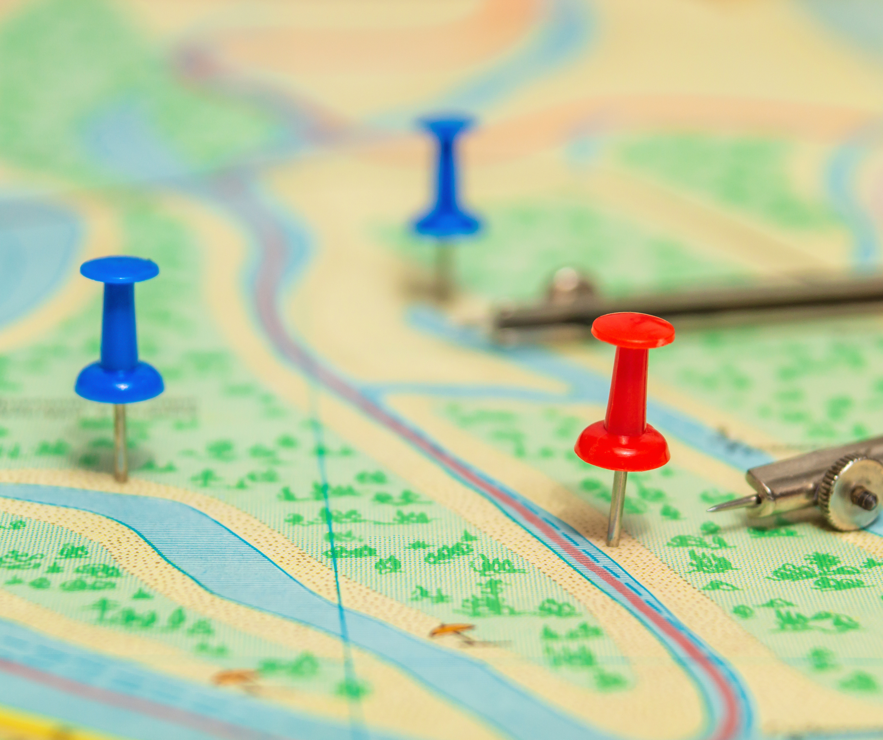 "Close-up of a map with blue and red push pins marking significant locations, accompanied by a compass tool."