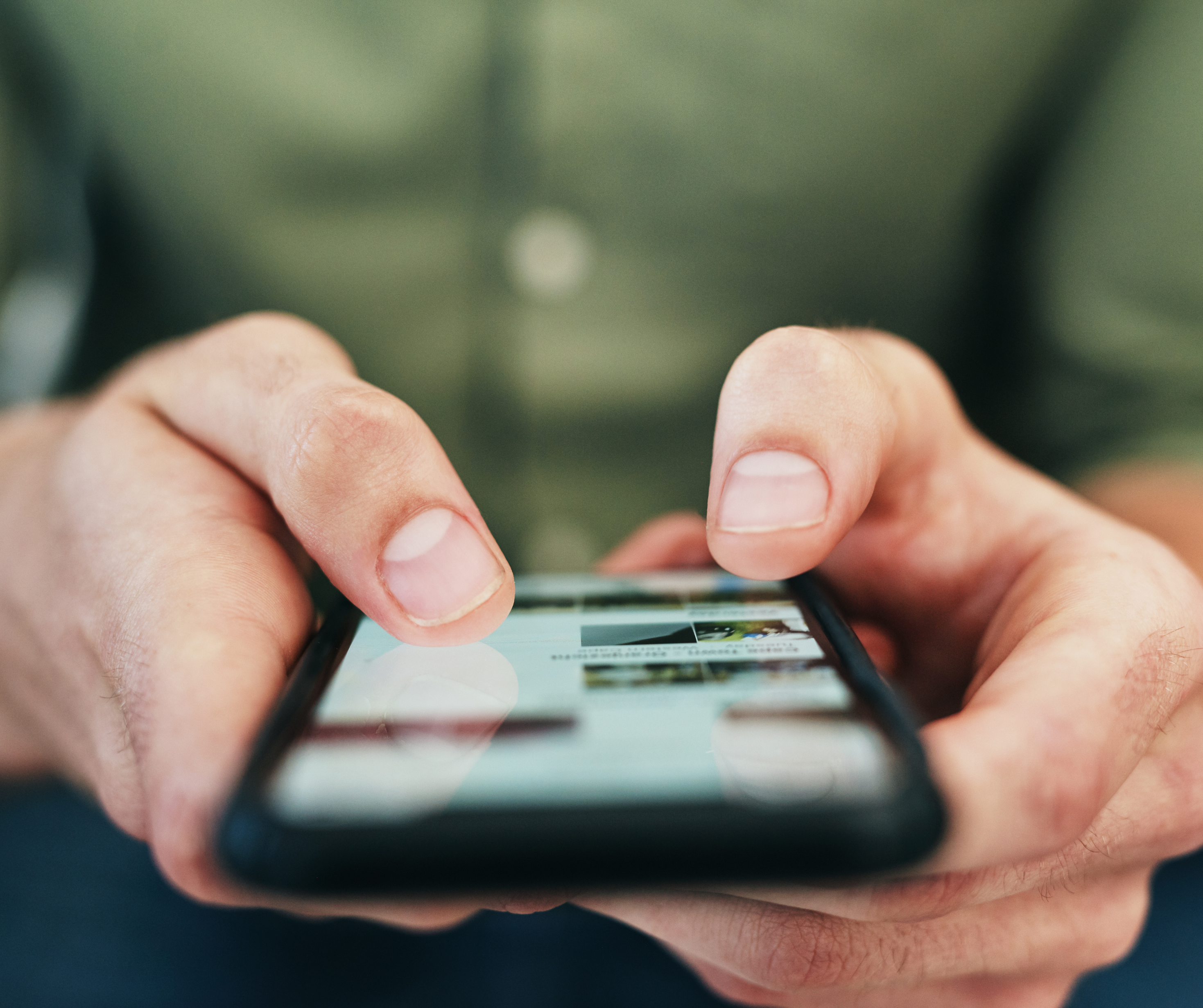 Close-up view of a personโs hands typing on a smartphone.
