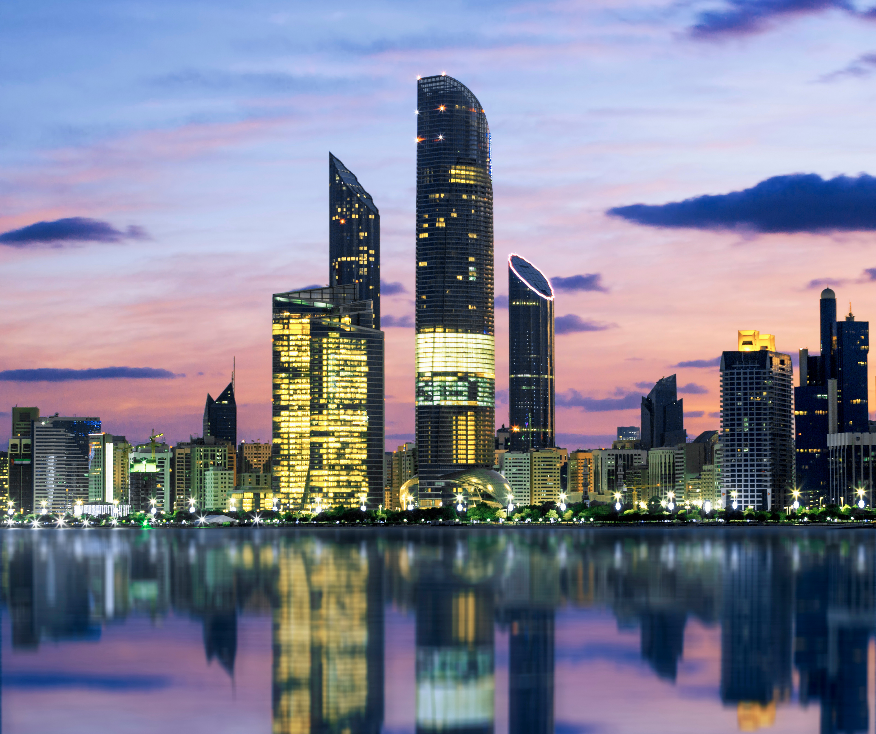 Abu Dhabi skyline at dusk with illuminated skyscrapers reflecting on the water.