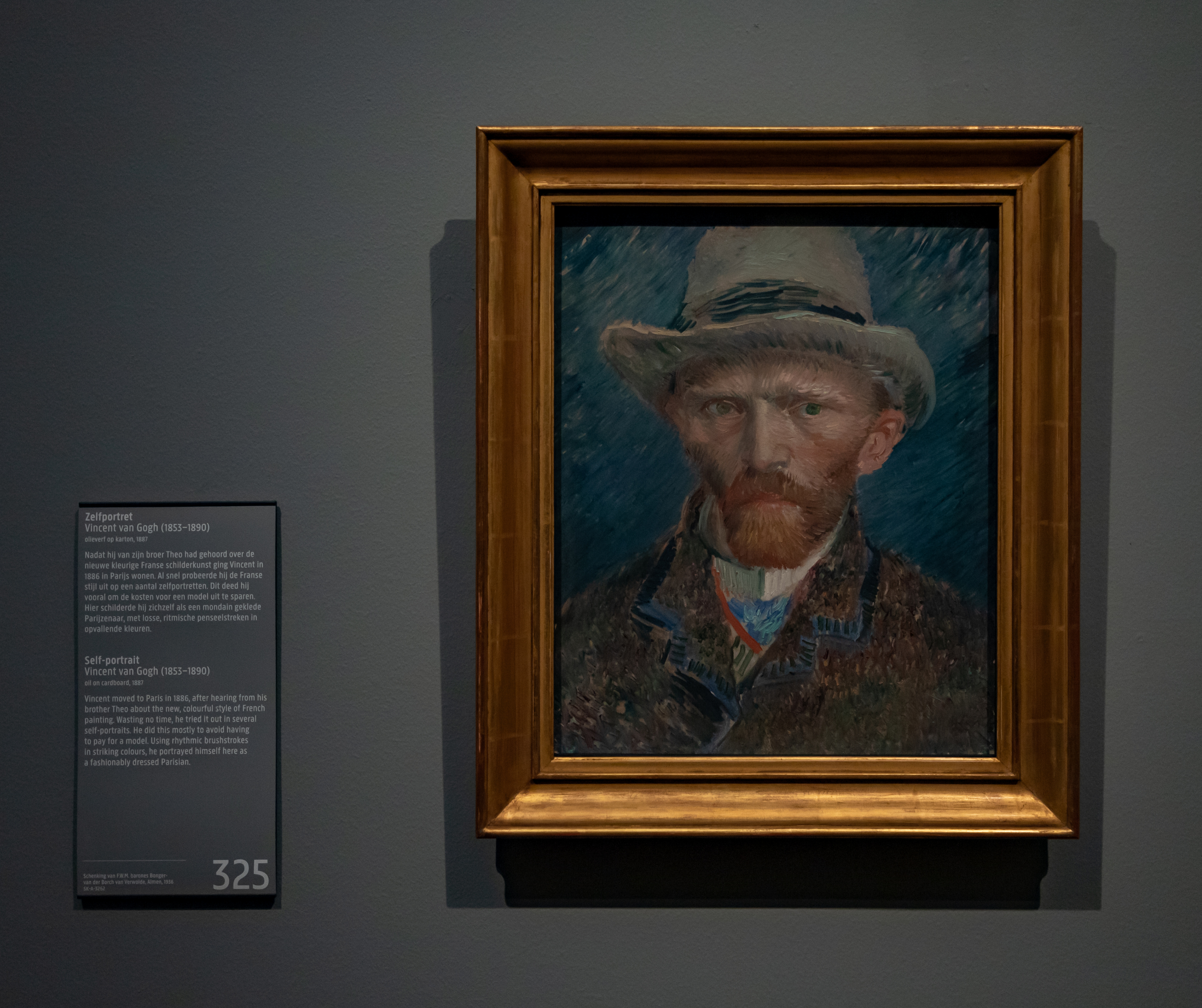 Self-portrait of Vincent van Gogh with a hat, displayed in a museum with an information plaque beside it.