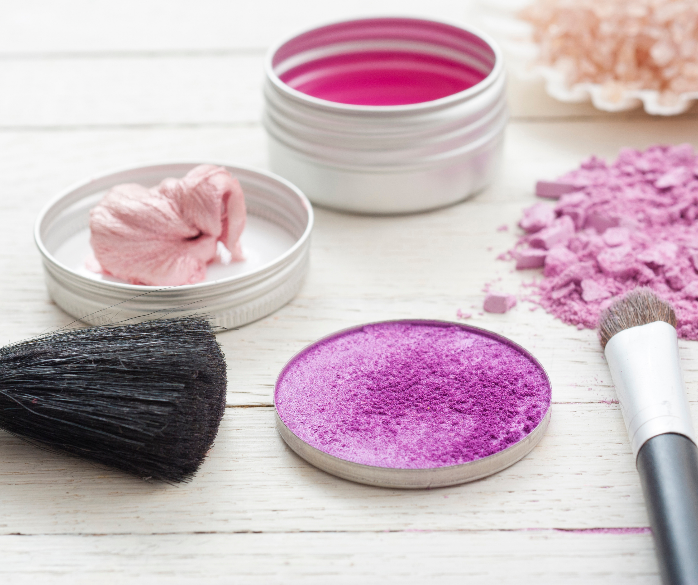 A table set with various makeup products including brushes, palettes, and mirrors, with participants practicing makeup techniques under the guidance of an instructor.