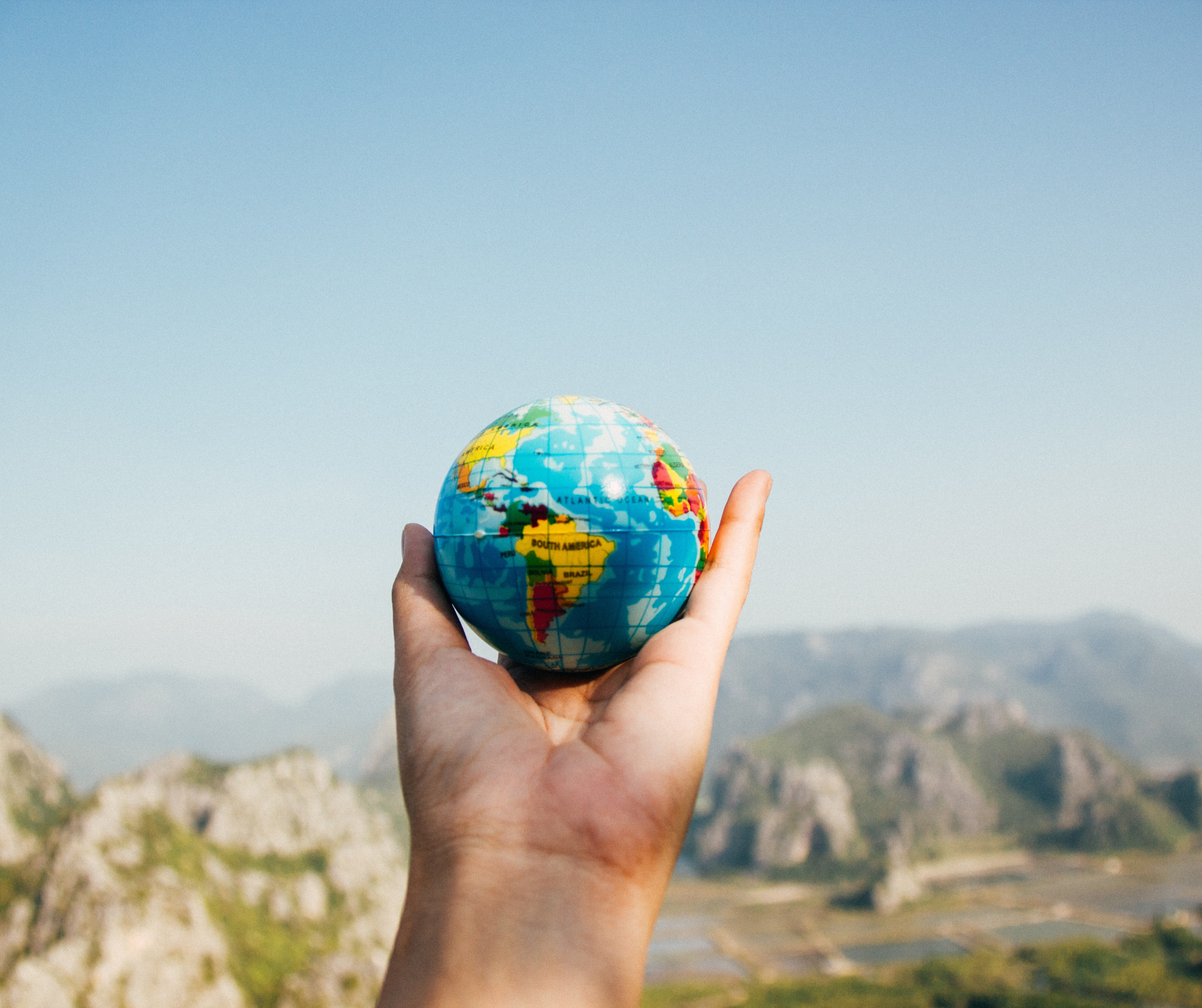 Hand holding a small globe with a scenic mountain background.