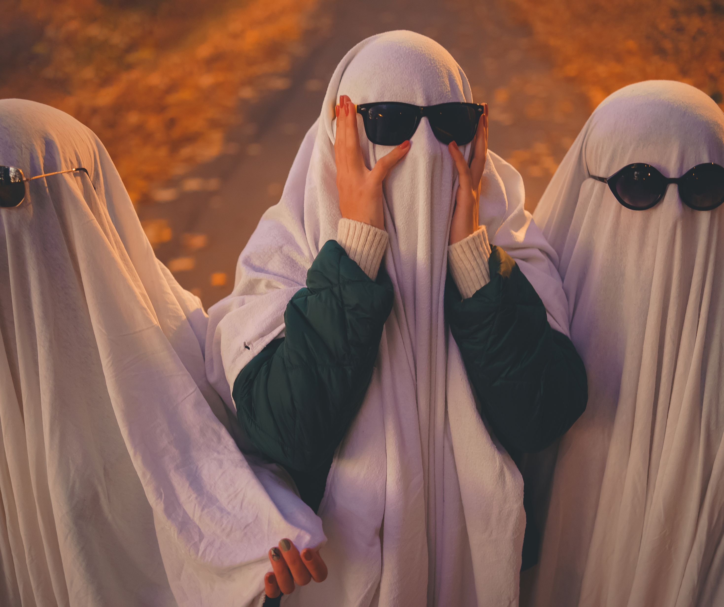 Three people dressed as ghosts wearing sunglasses on a New York street during Halloween.