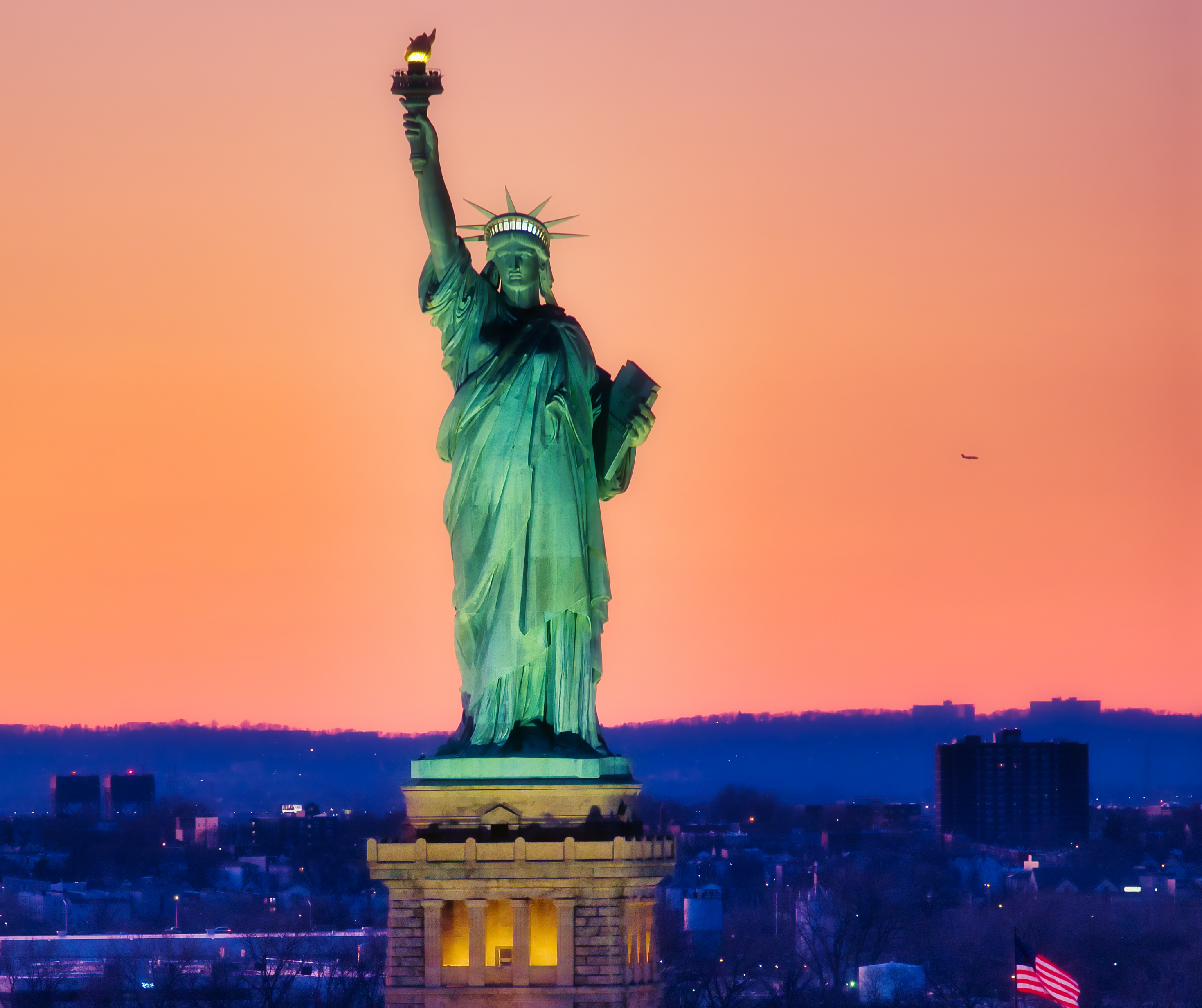 The Statue of Liberty against a vibrant sunset background.