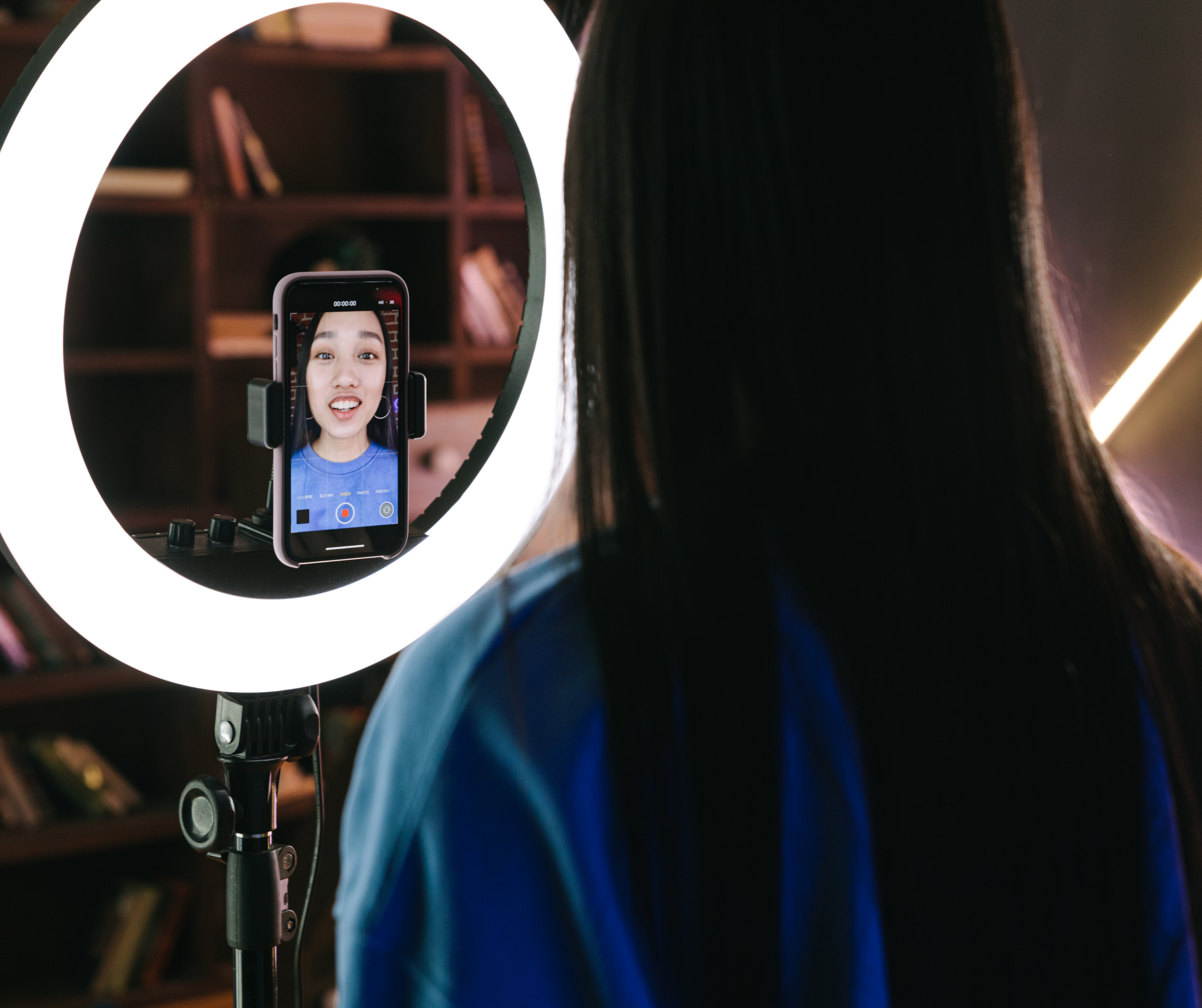 Young woman recording a video with a smartphone mounted on a tripod and illuminated by a ring light, representing collaboration with influencers.