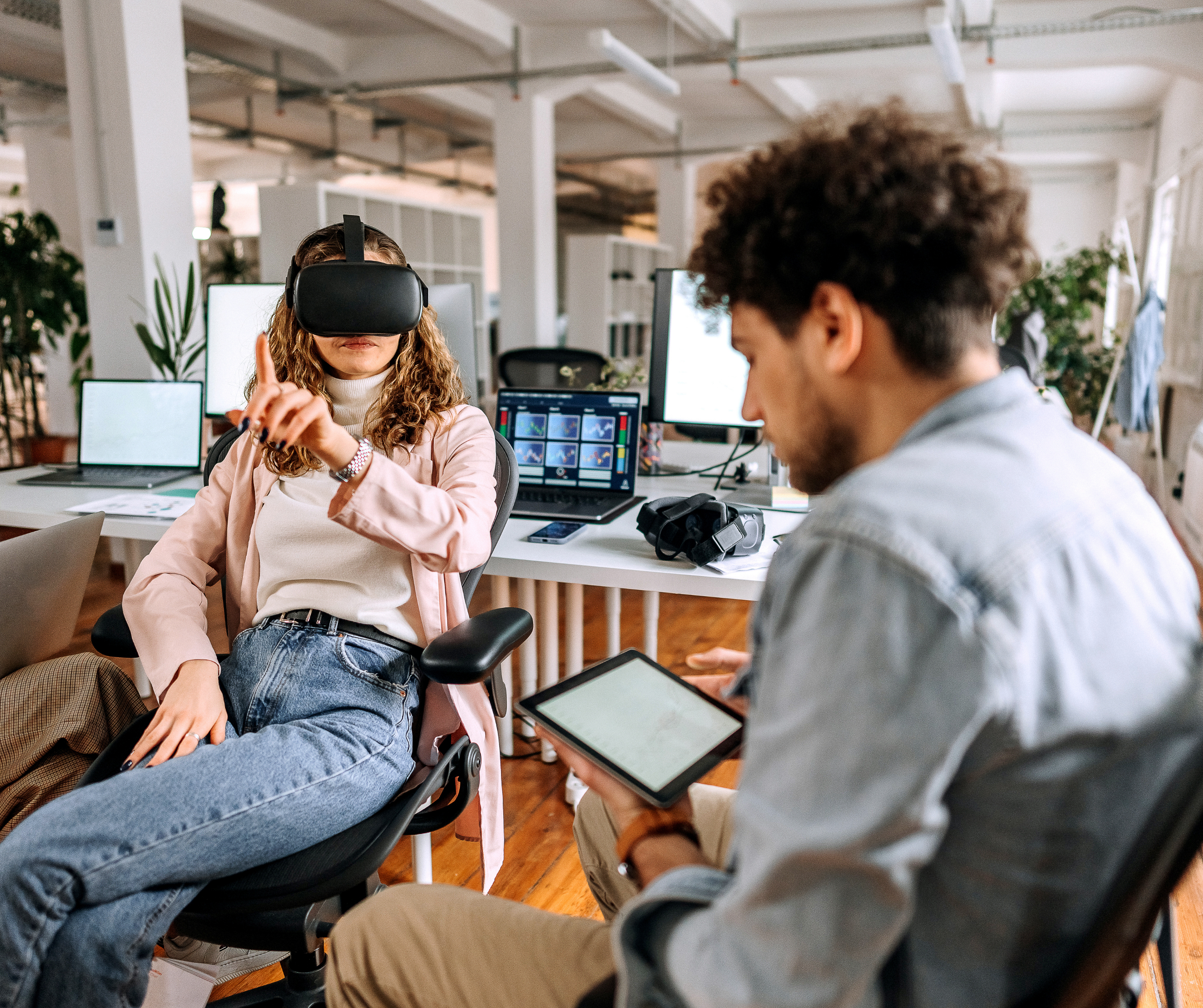 A woman sitting in an office chair wearing a VR headset, reaching out with one hand as if interacting with a virtual interface.