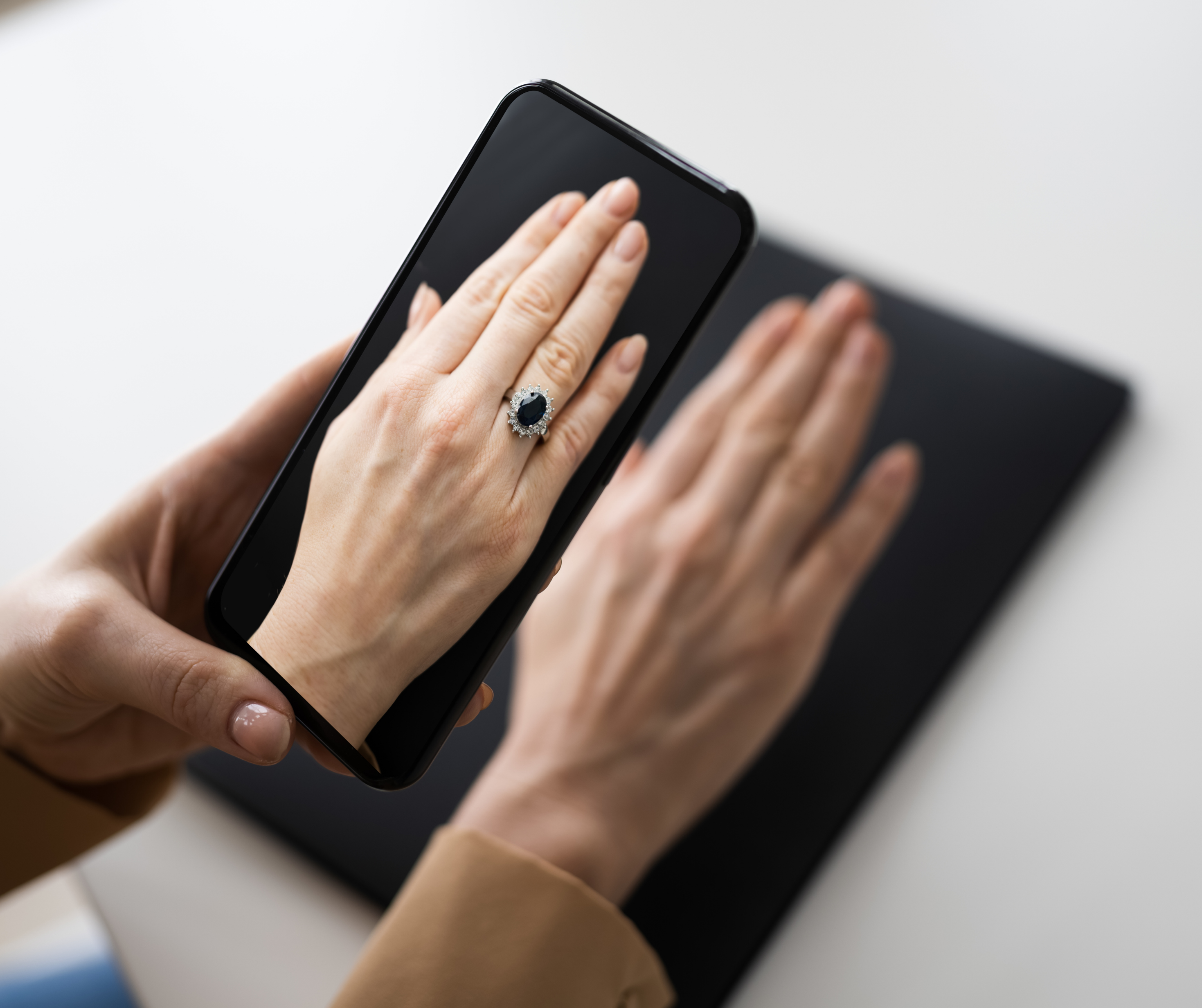 A person's hand holding a smartphone displaying an image of a ring on another hand, showcasing virtual shopping.