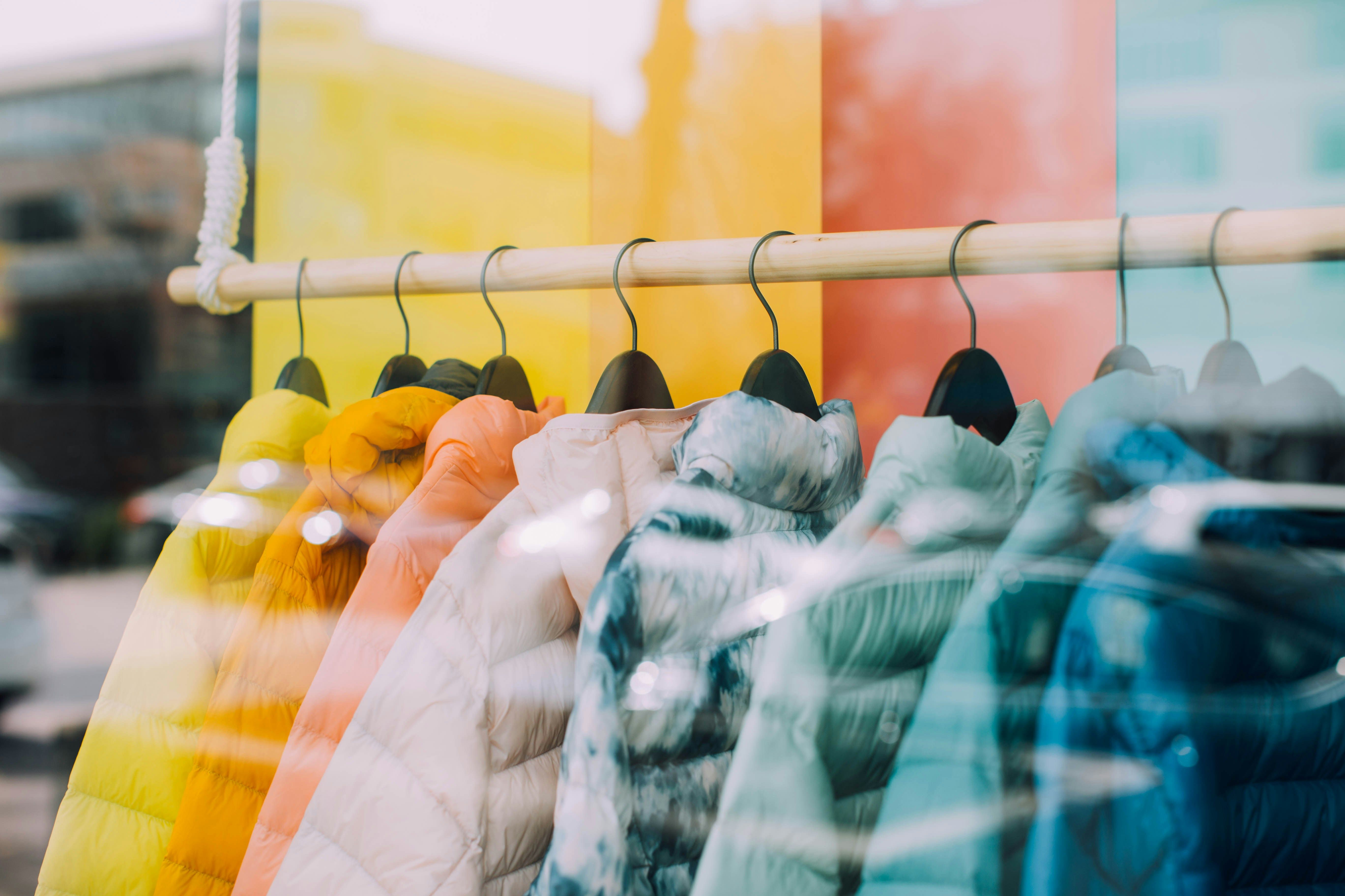 Clothing rack with puffy jackets in yellow, orange, pink, white, and blue colors against a multicolored background