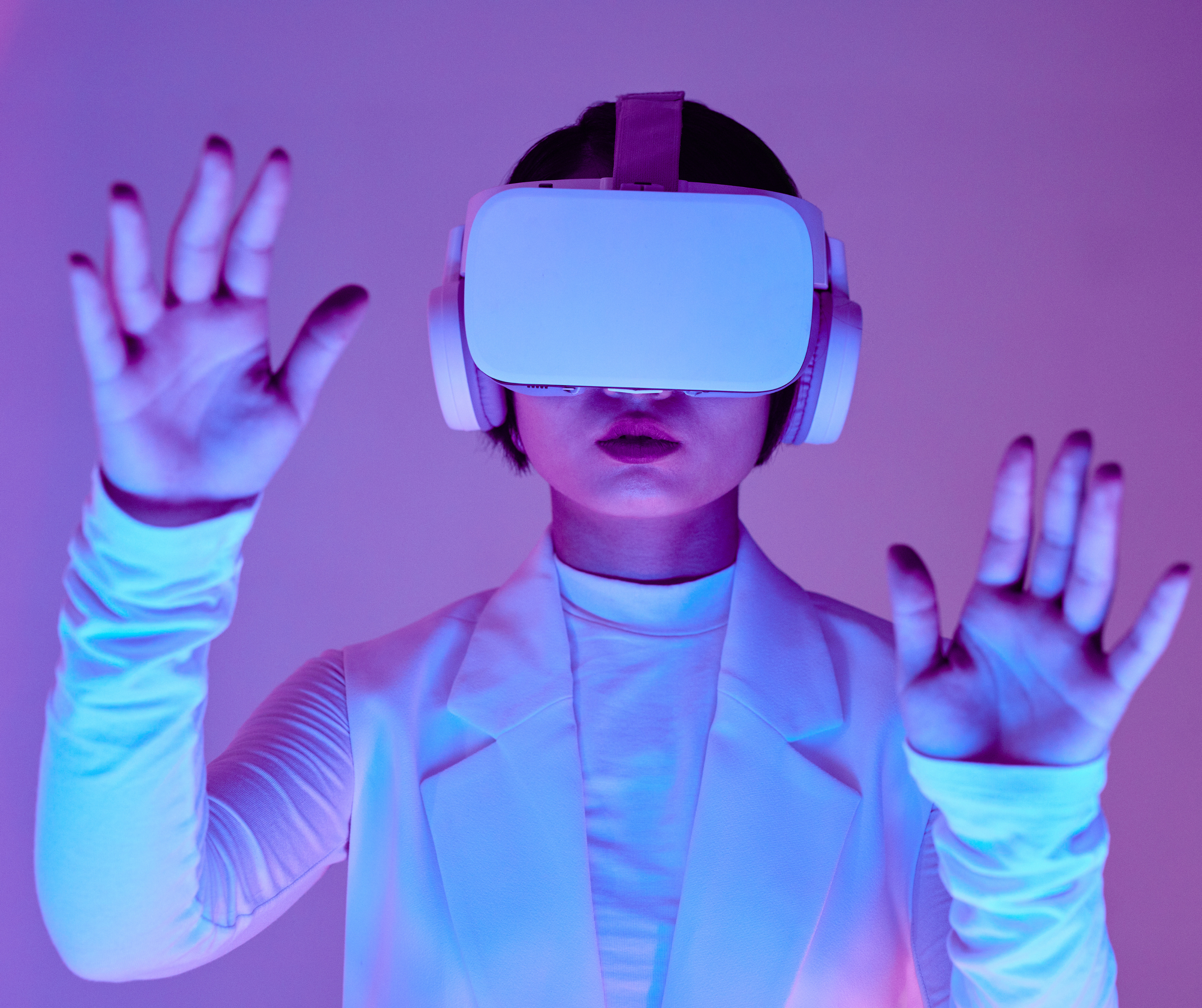 A woman wearing a VR headset and headphones, with her hands raised as if interacting with a virtual environment, bathed in colorful lighting.