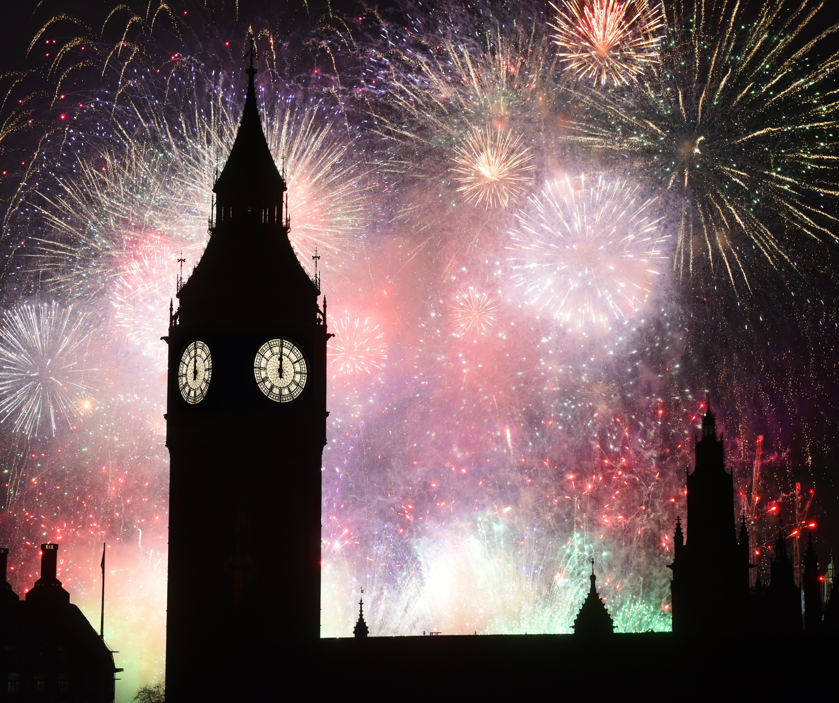 Big Ben clock tower silhouetted against a colorful fireworks display in London.