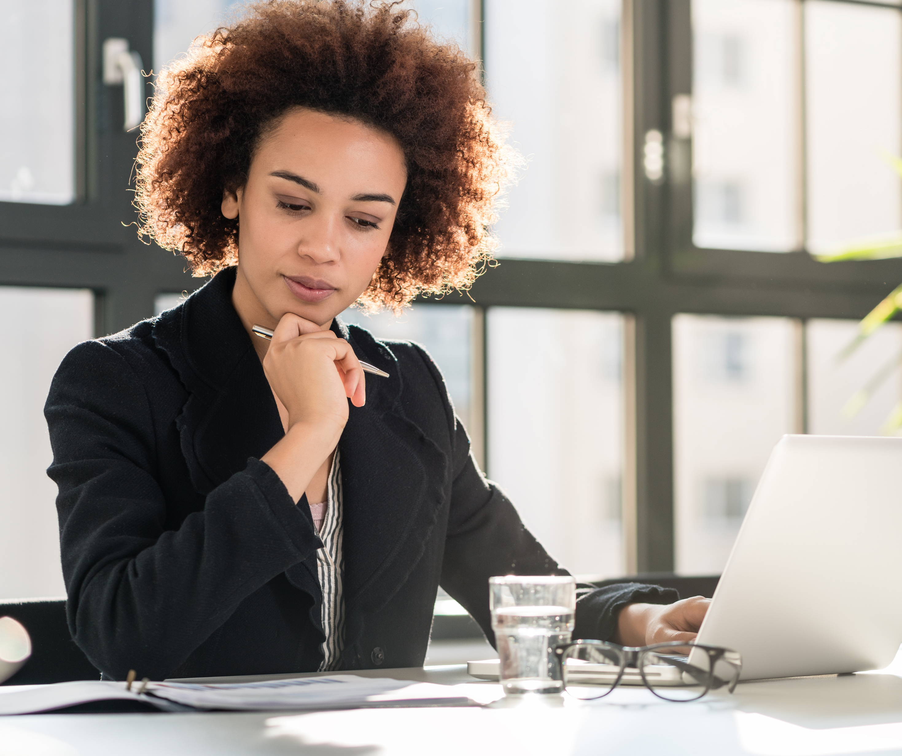 A woman sitting at a desk in a modern office environment, focused on analyzing data displayed on her laptop screen.