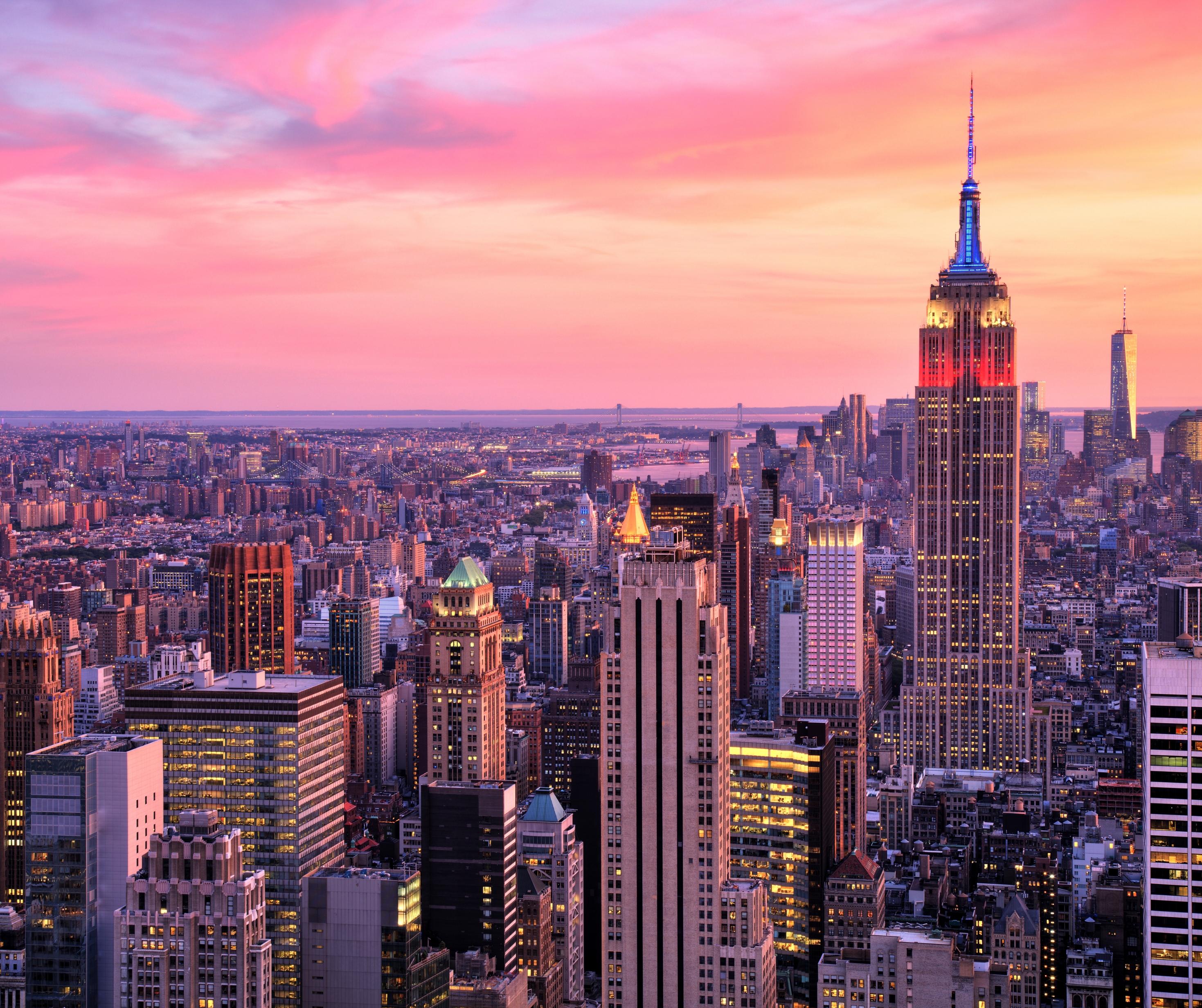 New York City skyline during sunset, featuring the Empire State Building and other skyscrapers under a pink and orange sky.