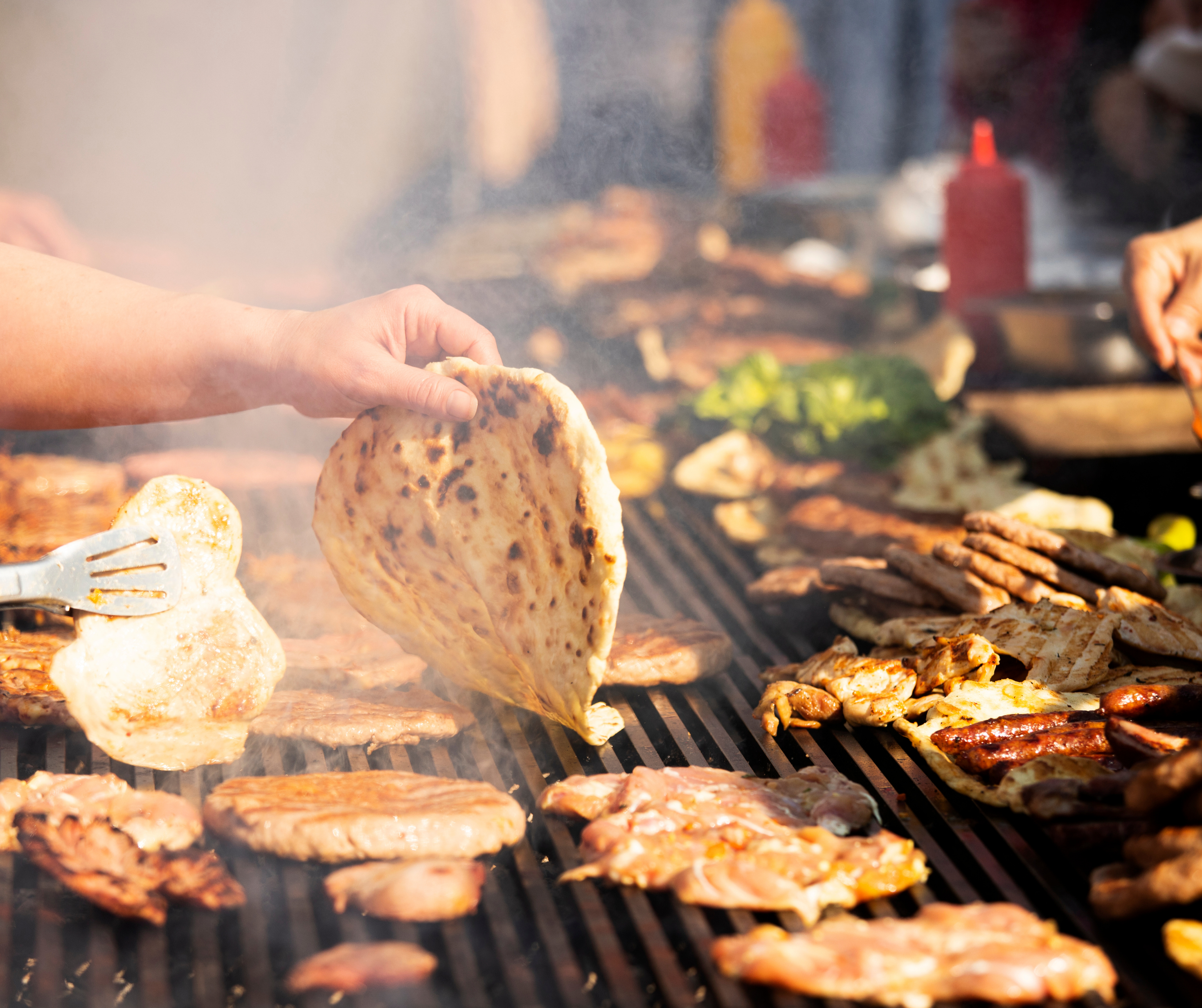 Outdoor barbecue with various grilled meats and flatbreads being prepared, showcasing the communal and diverse nature of pop-up dining experiences.