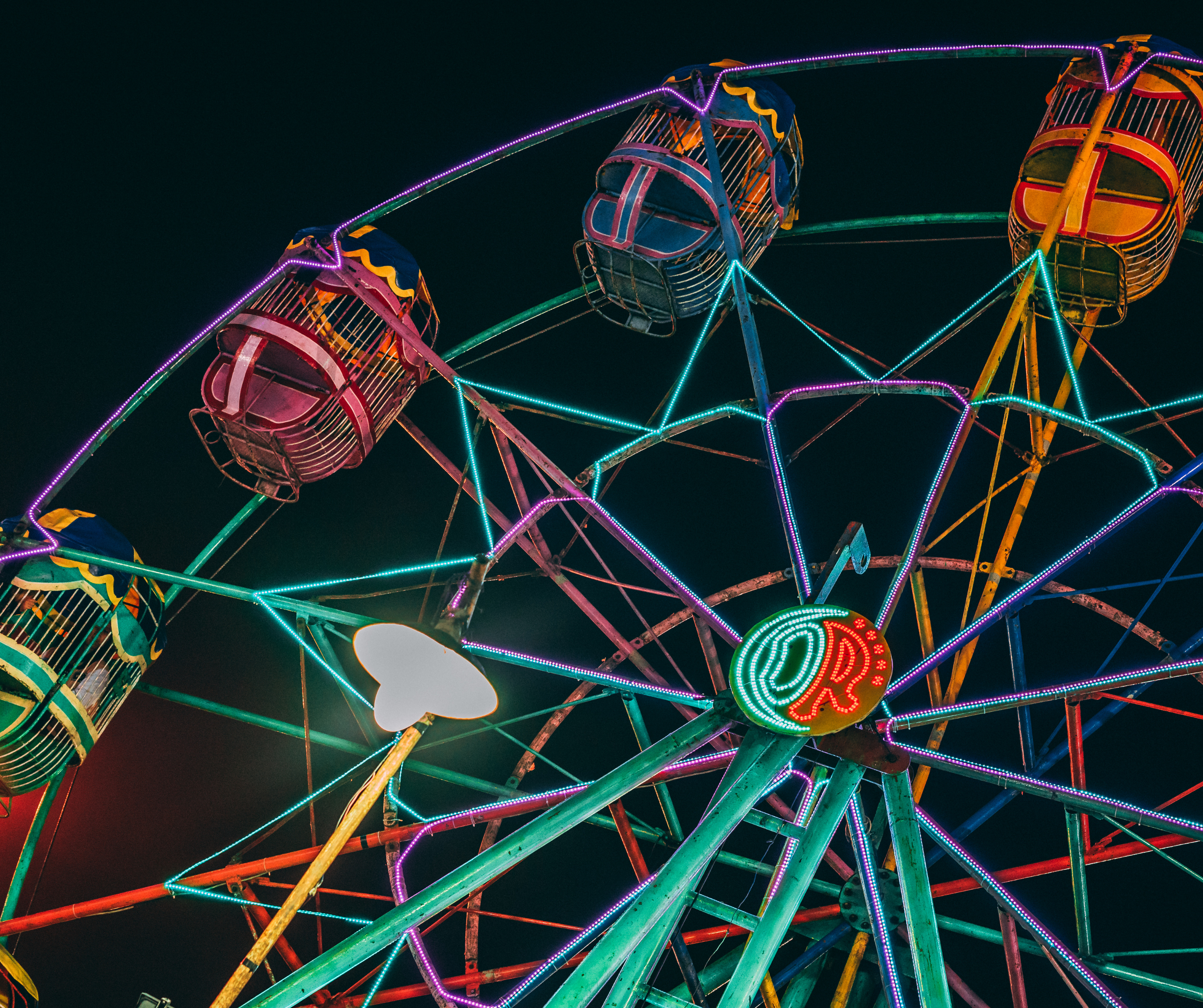  A Ferris wheel illuminated with colorful neon lights against a dark night sky.