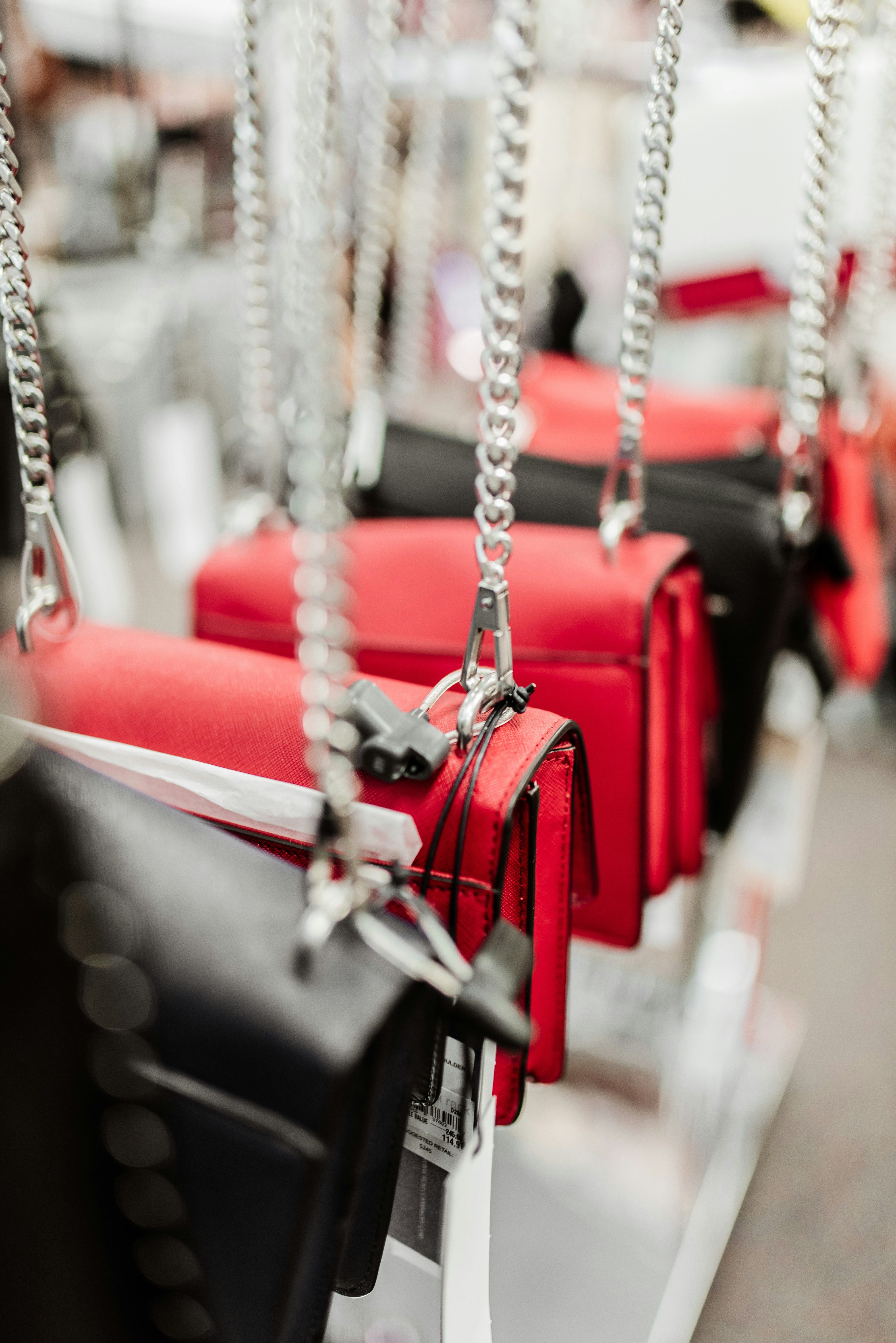 Multiple red and black handbags hanging from silver chains in a retail store